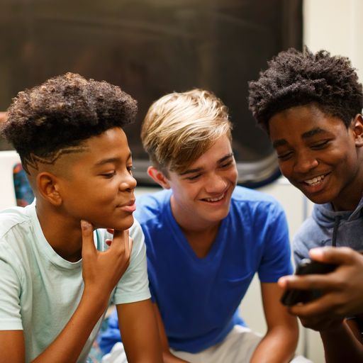 3 male students on a Metro train are smiling while looking at a smartphone
